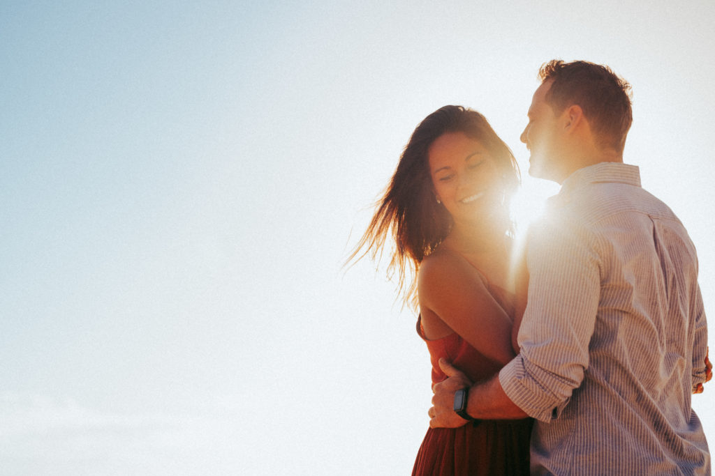 A woman and man are hugging each other at sunset during their engagement photo session