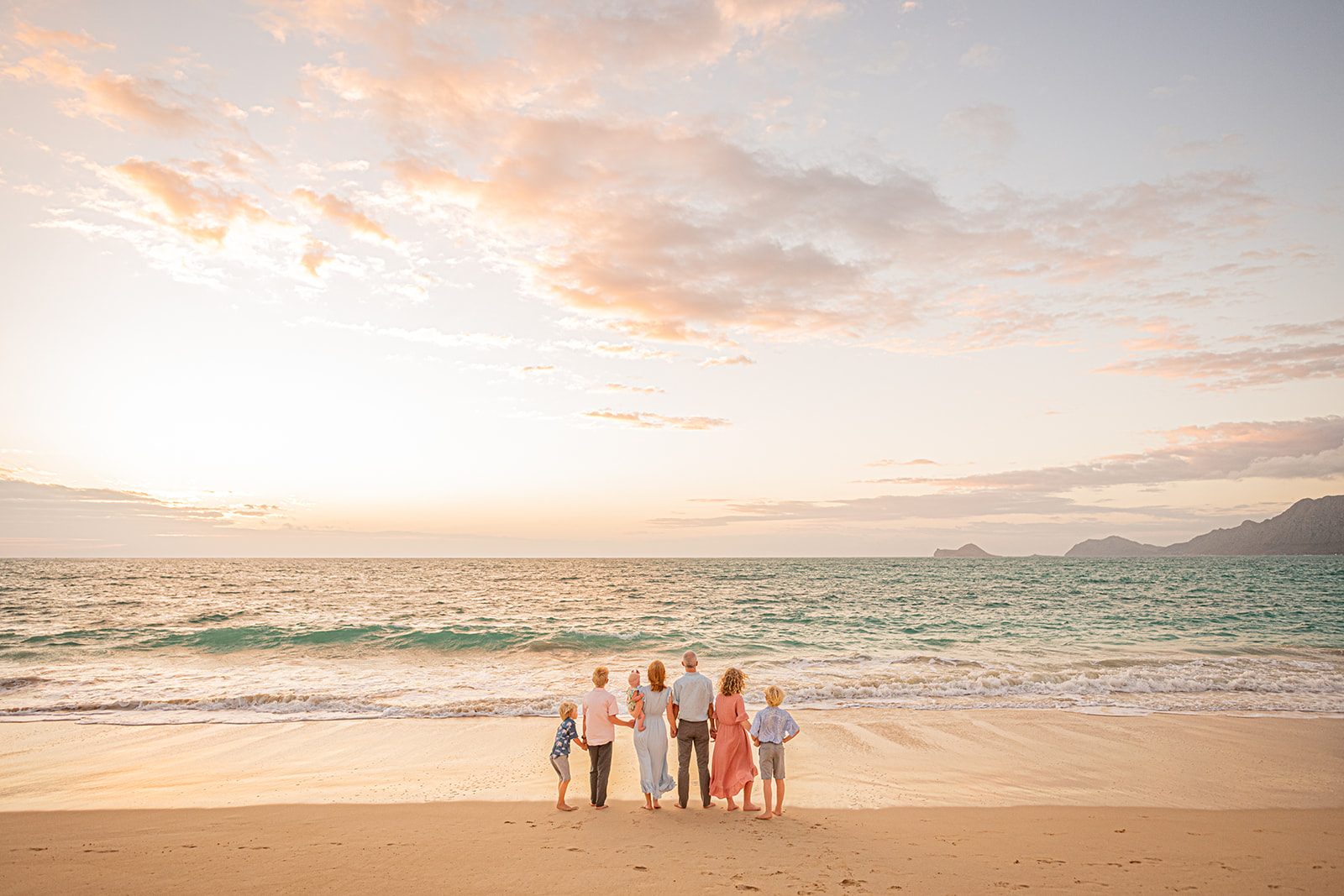 Family with their backs to the camera at the beach at sunrise