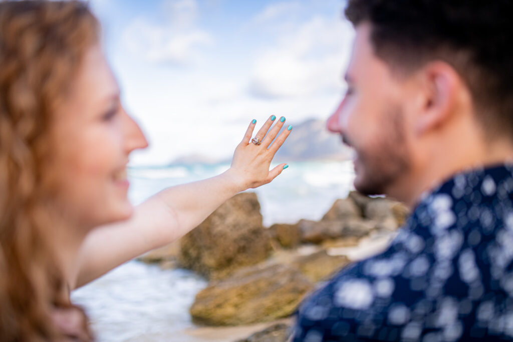 Woman and man are blurred while the woman's hand showing her ring finger with a ring on it is in sharp detail.