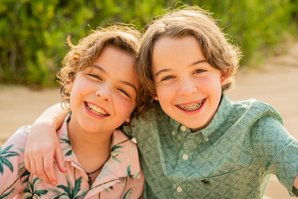 Brothers smiling while hugging on the beach at during their hawaii vacation photoshoot