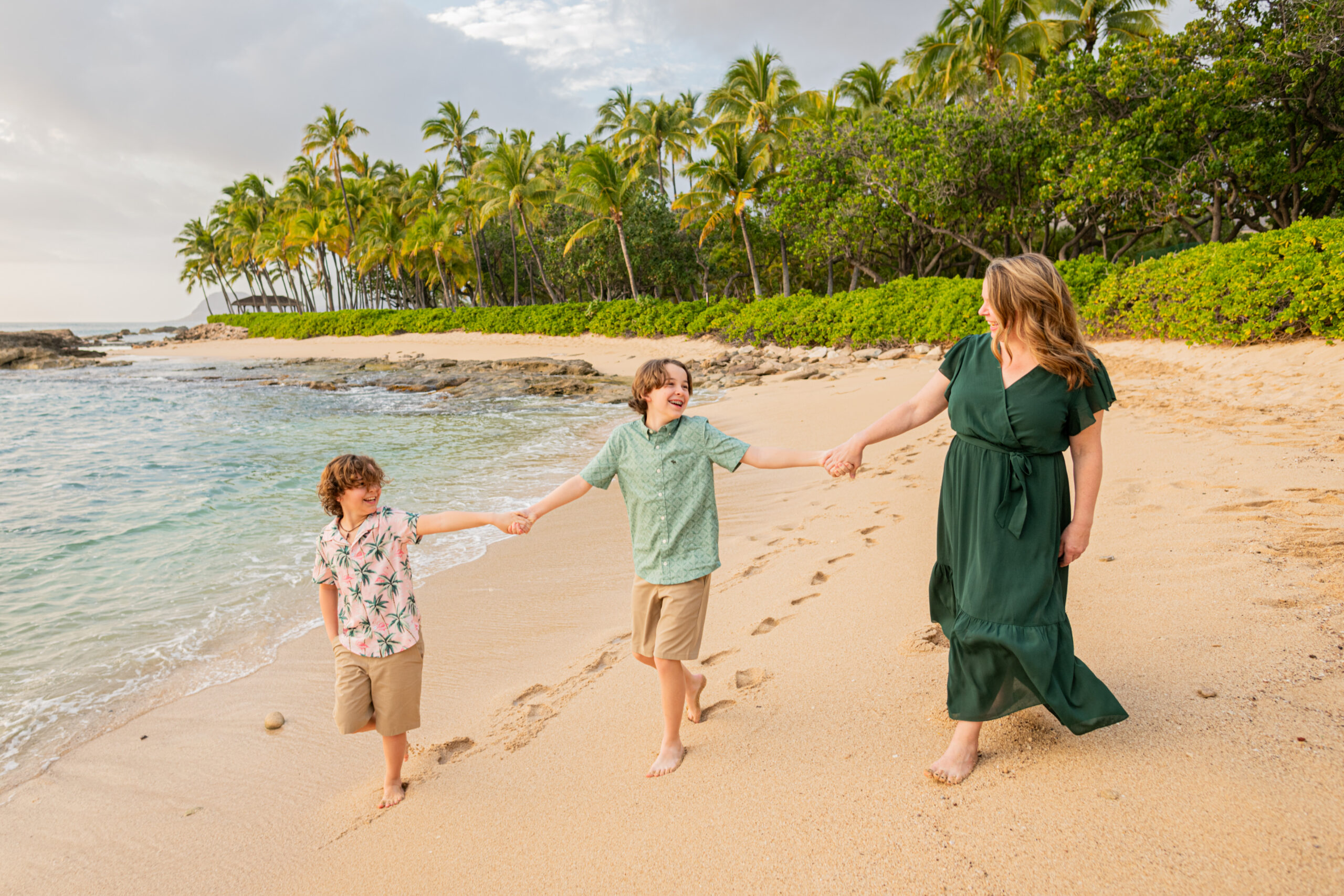 Mom and two boys are looking at each other on the beach during their Hawaii vacation photoshoot
