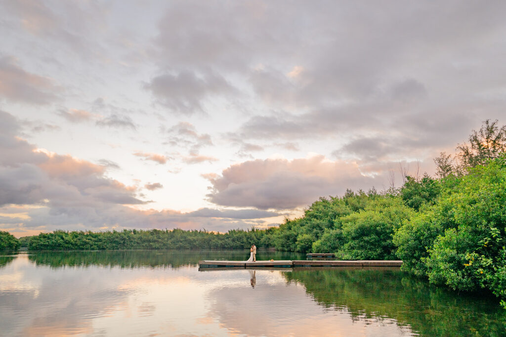 Husband and wife pose on the dock of a lake on Oahu's North shore